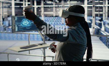 Data center IT expert investigates AI configurations using virtual reality, making adjustments for optimal function. Server hub engineer checks artificial intelligence error using VR headset, camera B Stock Photo