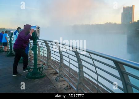 Visitors on the observation deck peer through binocular viewers toward the mist and skyline at sunrise. Stock Photo