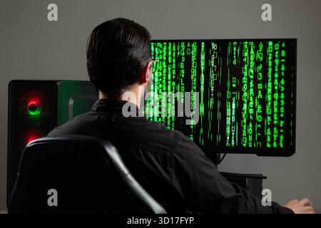 Close up to a man backward watching a computer monitor with a green matrix code on the screen Stock Photo