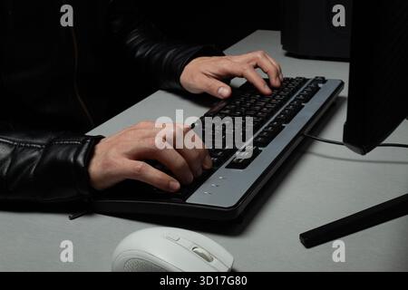 Close up to a male hands typing on a computer black keyboard with a white mouse on a hacker concept Stock Photo