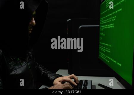 close up to a hooded hackerman writing a green html code into a computer keyboard Stock Photo