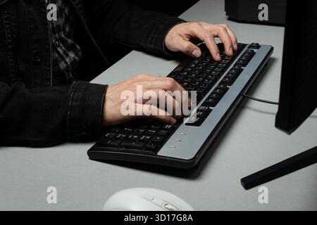 Close up to a male hands typing on a computer black keyboard with a white mouse Stock Photo