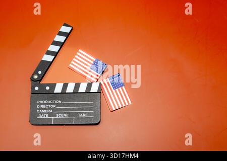 A clapboard sits with American flags on a vibrant orange background, representing filmmaking in the United States. Stock Photo