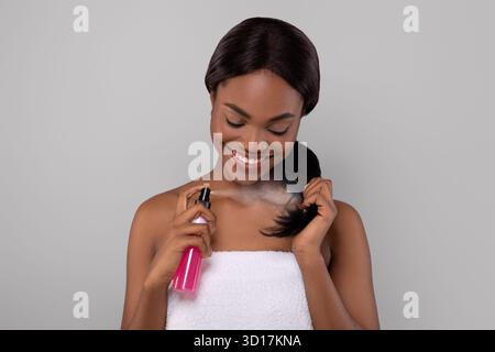 Smiling Woman Applying Hair Product While Enjoying Self-Care Routine Indoors Stock Photo