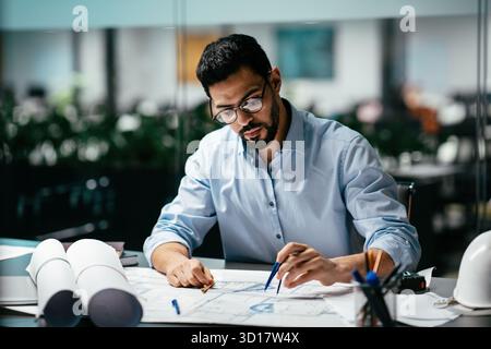 Man Working Diligently on Architectural Plans in a Modern Office Space During Business Hours Stock Photo