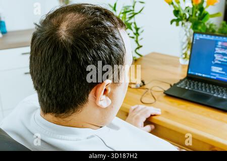 A man sits at a laptop and uses AI, seen from behind. High quality photo Stock Photo
