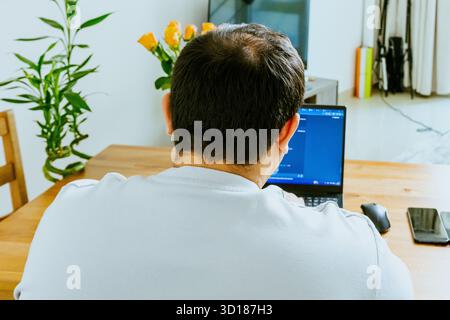 A man sits at a laptop and uses AI, seen from behind. High quality photo Stock Photo