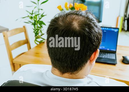 A man sits at a laptop and uses AI, seen from behind. High quality photo Stock Photo