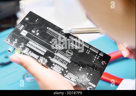 Close-up of a technician carefully soldering components on a printed circuit board in a well-lit workshop setting Stock Photo