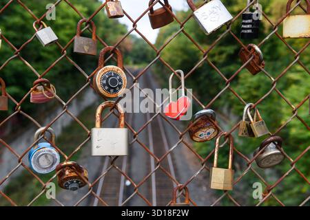 Old, rusted love locks or love padlocks on a cyclone fence along a railroad bridge, symbolizing the love shared between two partners. Stock Photo