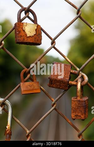 Old, rusted love locks or love padlocks on a cyclone fence along a railroad bridge, symbolizing the love shared between two partners. Stock Photo