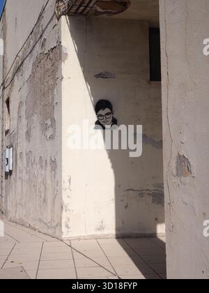 Street portrait on a weathered wall in Trapani with afternoon shadow falling across an old textured building Stock Photo