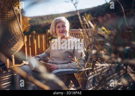 Portrait of smiling elderly lady relaxing on terrace during warm autumn day. Stock Photo