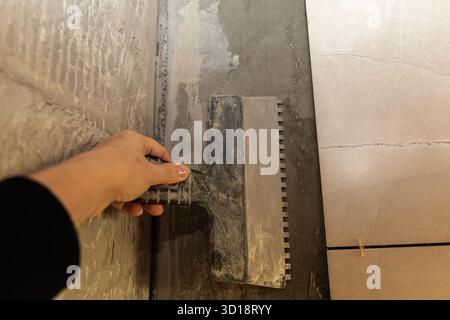 Worker applying tile adhesive on wall with notched trowel during renovation Stock Photo