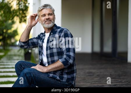 Gray-haired mature man sitting in his house yard and having morning coffee Stock Photo