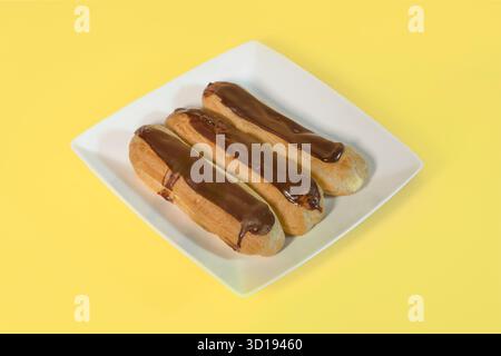 On a lemon background, three eclairs are arranged on a white plate Stock Photo