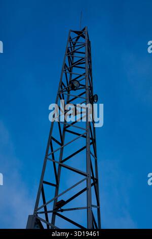 Metal communication antenna tower with geometric structure against blue sky. Stock Photo