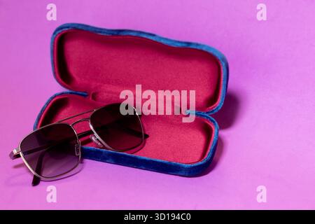 Elegant designer sunglasses with dark tinted lenses leaning on open velvet case, set on pink purple gradient surface for modern product display Stock Photo