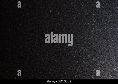 Dark metallic glitter texture illuminated softly from right, macro focus highlights subtle sparkles shimmering across abstract granular relief Stock Photo