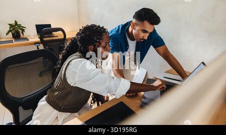 Two architects, a man and a woman, collaborating in a modern open office, reviewing architectural designs on a laptop, showcasing teamwork, project pl Stock Photo