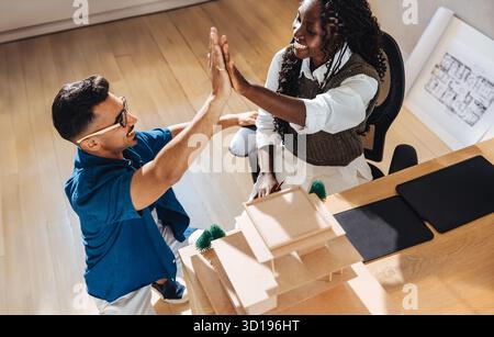 Two young professionals, a male architect and a female colleague, exchange a high-five in a collaborative studio setting, showcasing creativity, teamw Stock Photo
