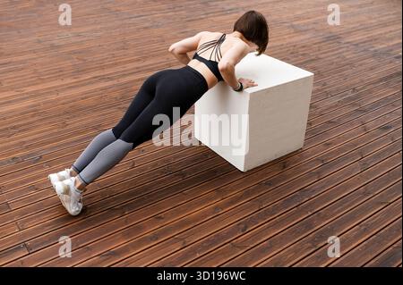 Sportswoman doing push ups on cube on wooden area Stock Photo