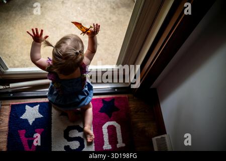 Overhead View of Baby Girl Looking Out Front Door with Toy Stock Photo