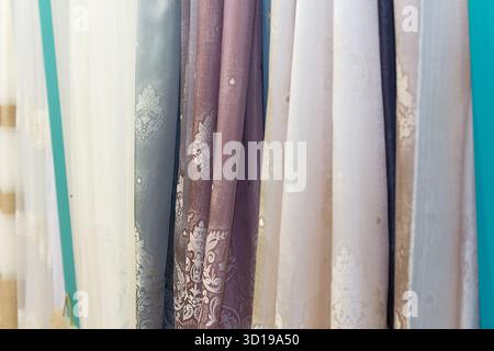 Decorative transparent curtains with floral and ornamental patterns, multicolored textile samples hanging vertically on the showcase. Home decor Stock Photo