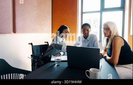 Professionals of diverse ages and backgrounds engage in teamwork inside a contemporary office setting, using technology and collaboration to achieve g Stock Photo