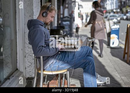 Remote worker. Man working with a laptop computer on a street pavement. England, UK Stock Photo