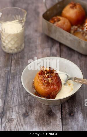 Baked apples in a tin and in a bowl, served with vanilla custard Stock Photo