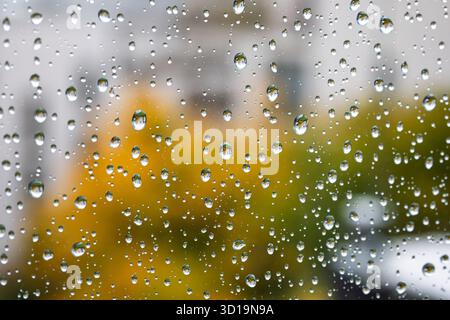 Rain drops flowing down a large home window with blurry fall colored trees in the background. Close up view, shallow depth of field, moody, no people Stock Photo