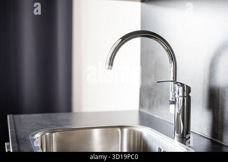 Closed, new, stainless water tap faucet and sink in apartment kitchen. Bright, natural window light, selective focus, no people Stock Photo