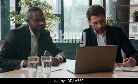 Multiracial business men office team businessmen guys talking writing notes in documents signing papers African American Caucasian colleagues working Stock Photo