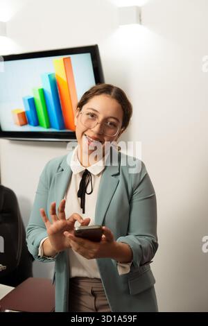 Young businesswoman smiling, using a mobile phone with a bar chart on screen in a modern office Stock Photo