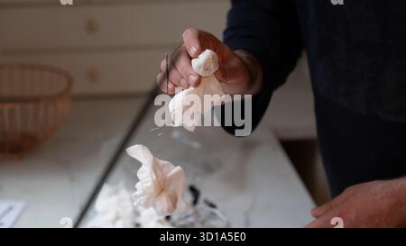 Close-up of a person holding small handmade ghost decorations crafted from white fabric and thread. Homemade Halloween decor idea made with simple mat Stock Photo