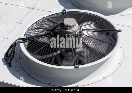 Industrial cooling fan unit on roof with protective grill. Stock Photo