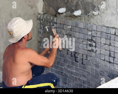 Badung, Bali, Indonesia – October 26, 2025: A construction worker installing small mosaic tiles on a wall using cement mortar and hammer Stock Photo