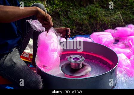 Person Making Pink Cotton Candy On Outdoor Spin Machine At Market Stall During Sunny Day Stock Photo