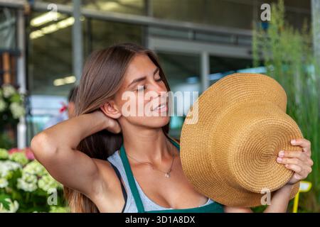 Woman feeling heat, fanning herself with a straw hat outdoors in a gardenhouse Stock Photo