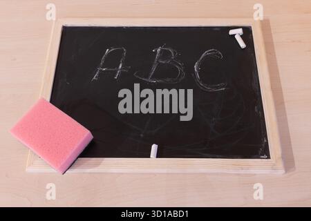 Top view of blackboard with pink sponge and white chalk. On blackboard written A B C letters Stock Photo