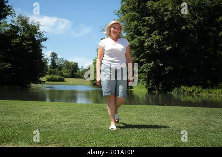 Confident Blonde Woman Walking in Nature Park Stock Photo
