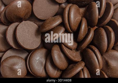 A detailed close-up (macro) photograph of a pile of smooth, rich brown chocolate chips or callets. The image highlights the texture and form of the in Stock Photo
