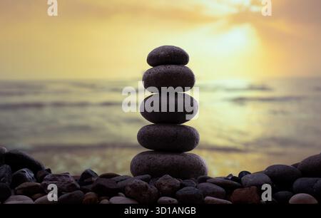 Stack of smooth stones balanced on the beach at sunset, symbolizing harmony, balance, and mindfulness. Stock Photo