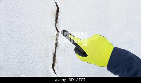 Man with yellow glove hand finger pointing to cracked ceiling. Building problem and solution concept. Close up Stock Photo