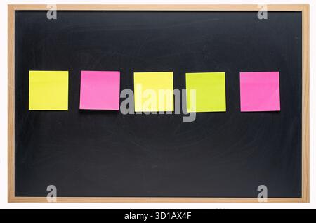 Stacks of multi-colored square paper sticky notes on a blackboard, close-up Stock Photo