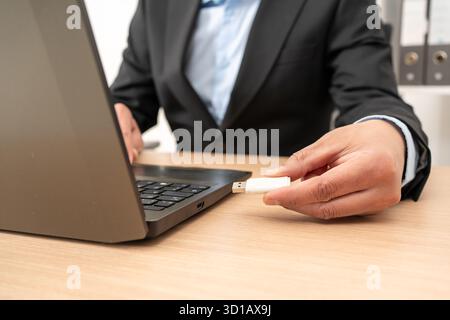 Businessman hand plugging pen drive on laptop at office Stock Photo