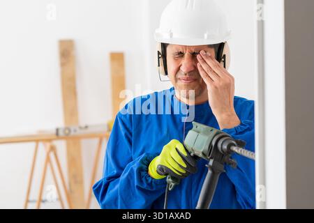 Construction worker suffering accident in an eye working with a electric drill without protection glasses at building Stock Photo