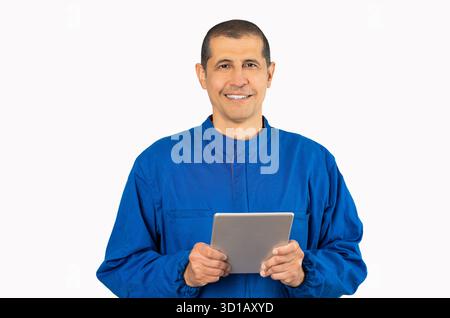 Confident smiling professional handyman in blue overalls using digital tablet against a white background. Stock Photo