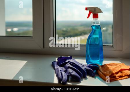 Cleaning spray, cloth and gloves placed on a windowsill, preparing for window washing and household chores Stock Photo